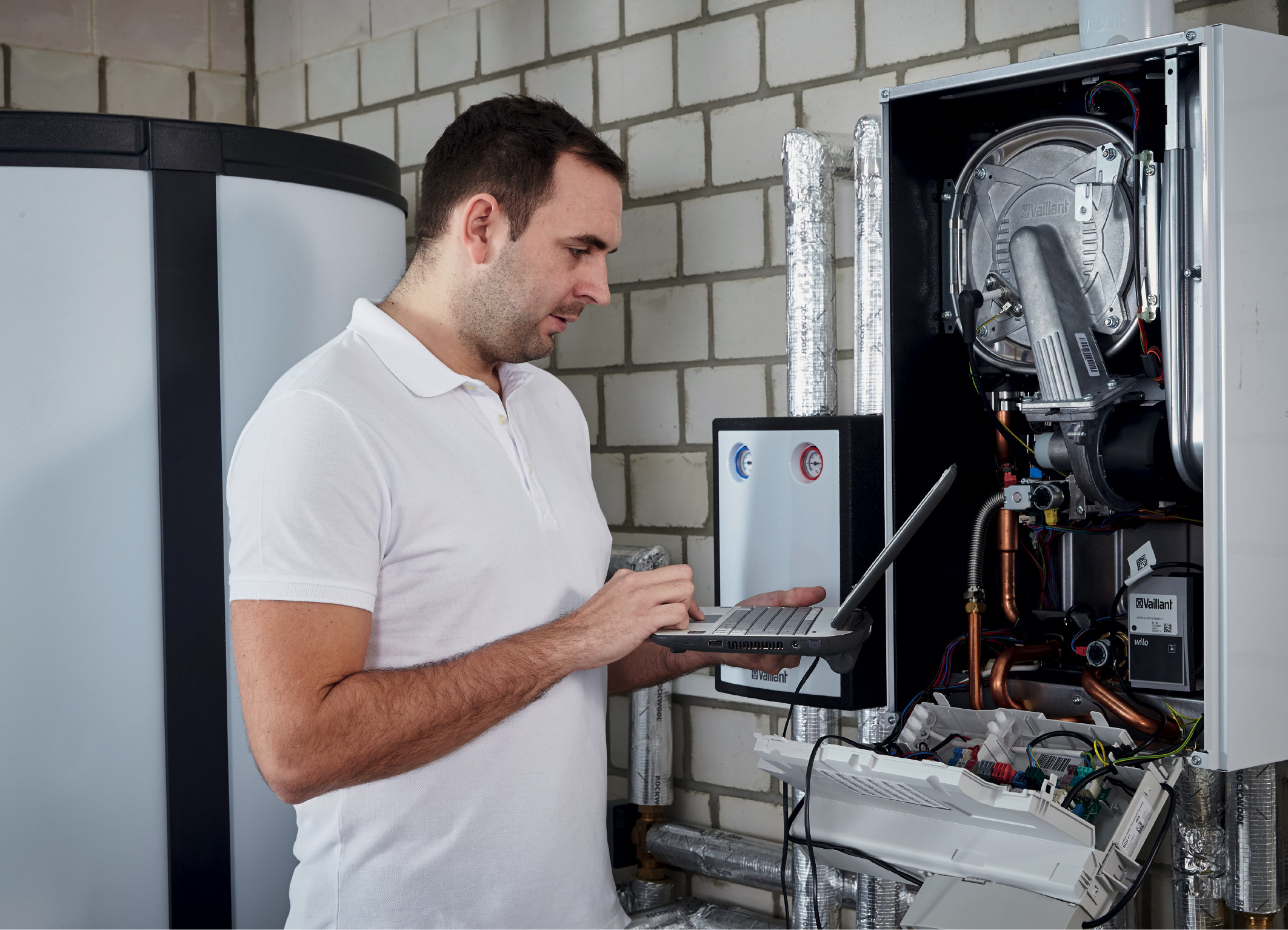 ein Techniker steht mit seinem Laptop vor der geöffneten Heizungsanlage